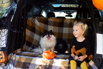Cute girl sitting with dog in car trunk