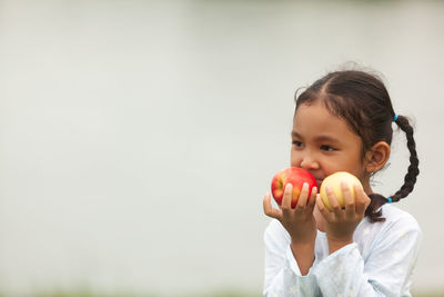 Portrait of cute girl holding apple against white background