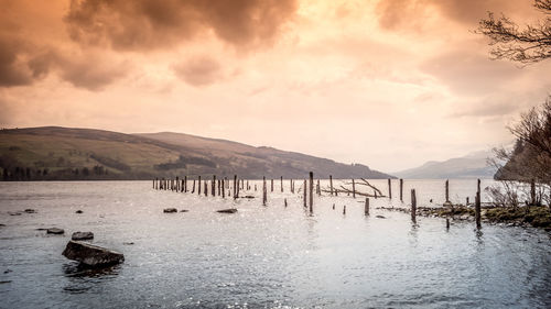 Wooden posts in lake against sky