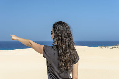 Rear view of woman standing at beach against clear blue sky