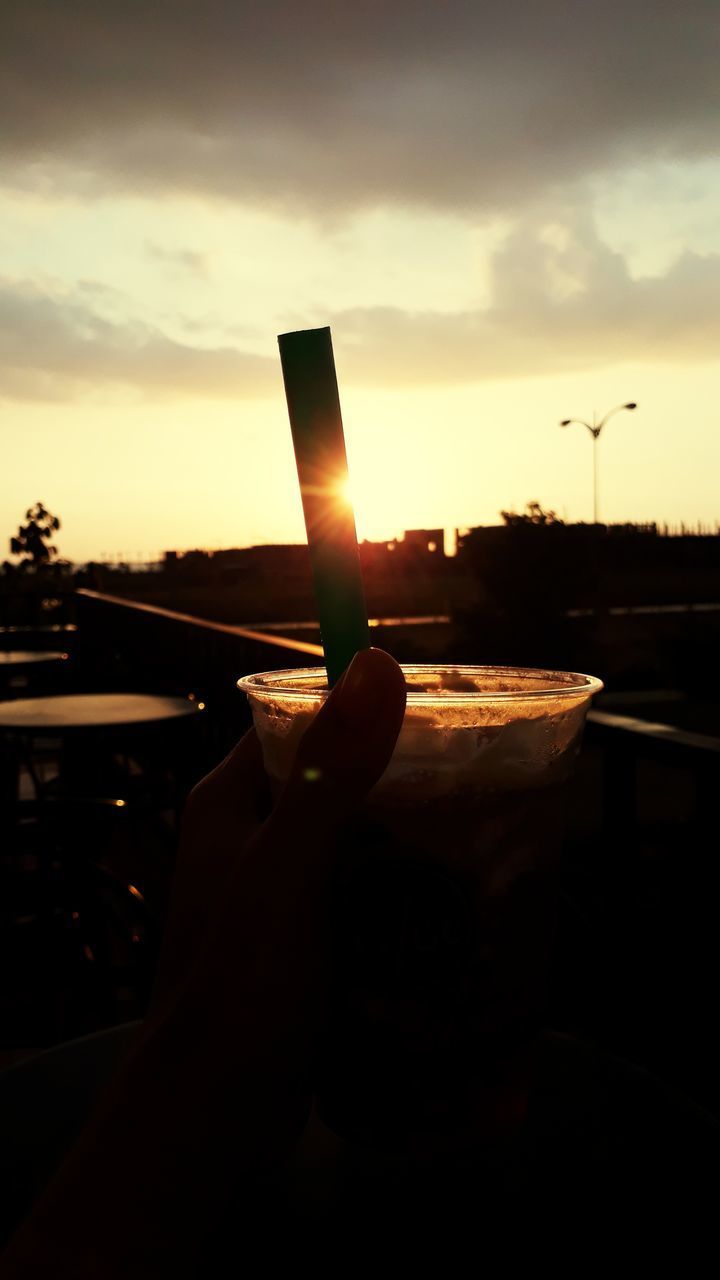 CLOSE-UP OF HAND HOLDING SUN AGAINST SUNSET