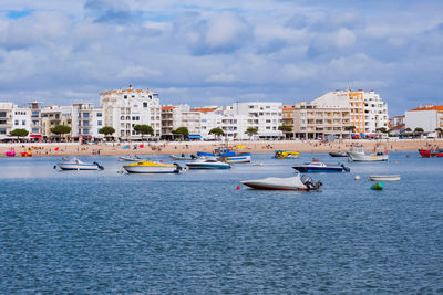 Boats moored on sea by buildings in city against sky