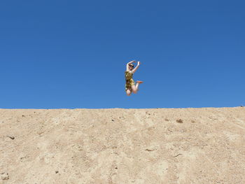 Girl jumping in desert against clear blue sky