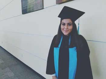 Portrait of young woman wearing graduation gown while standing by building