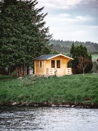 House by river amidst trees and building against sky