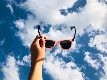 Low angle view of hand holding sunglasses against sky