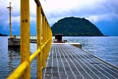 Yellow railing of pier over river against sky