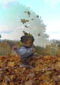 Boy in autumn leaves on field against sky