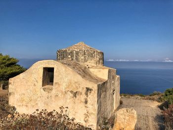 Old building by sea against clear blue sky