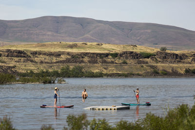 A young man jumps off a dock while friends on sups watch nearby.