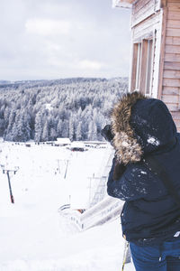 Rear view of person photographing on snow covered field against sky