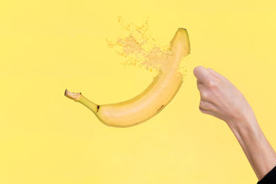 Digital composite image of hand by banana against yellow background