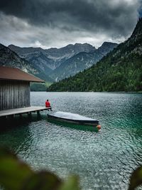 Man sitting on pier over lake against mountains