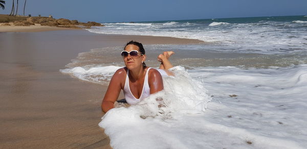 Full length of overweight woman wearing bikini lying on shore at beach during sunny day