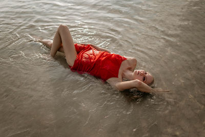 Girl in a red dress lies in sea water
