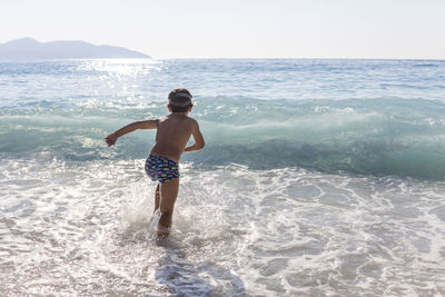 Full length of shirtless boy on beach against sky