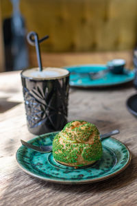 Pistachio eclair, profiterole in glaze on green plate on table, close up. eclair