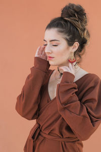 Girl with eyes closed standing against orange background