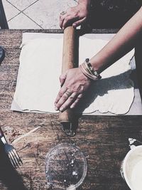 Cropped hands of woman rolling dough at table