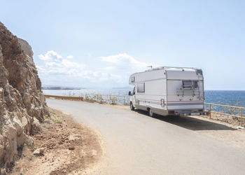 Motor home on road by sea against sky during sunny day