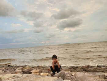 Portrait of boy crouching at beach against sky