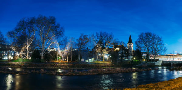 River by illuminated buildings against blue sky at night