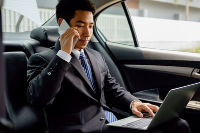 Businessman using mobile phone and laptop in car