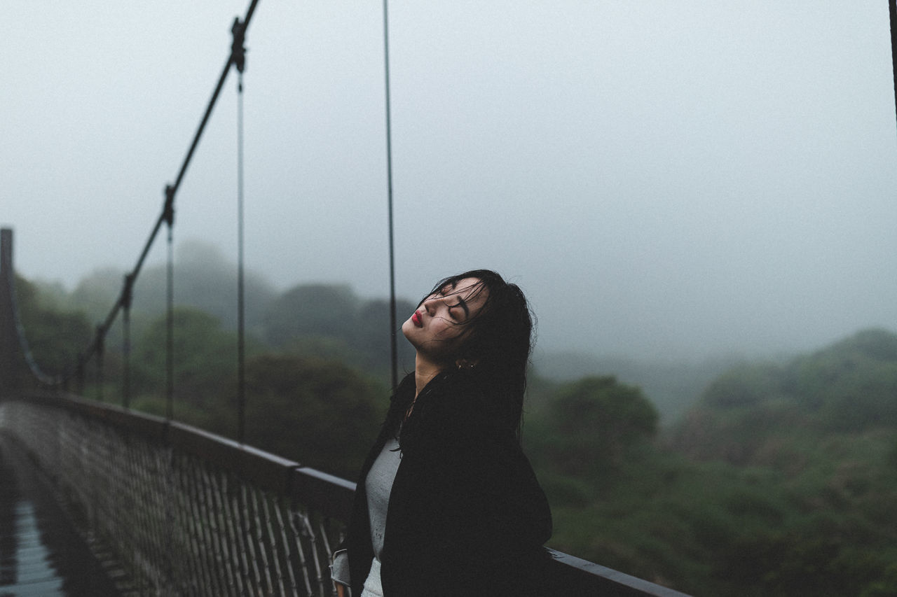 one person, real people, young adult, lifestyles, leisure activity, young women, standing, focus on foreground, looking, fog, nature, railing, sky, day, side view, looking up, adult, women, outdoors, hairstyle