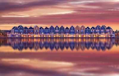 Reflection of illuminated houses on lake against cloudy sky