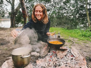 Portrait of smiling young woman preparing food on barbecue grill or bonfire