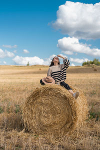 Woman sitting on hay bales on field against sky