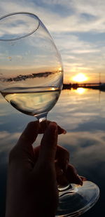 Close-up of hand holding glass against sky during sunset