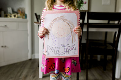 Young girl holding a drawing she made of her mom for mother's day