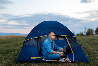 Young male freelancer is working on a laptop outdoors in mountains. freelance concept.