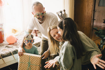 Cheerful parents and boy giving birthday present to girl at home