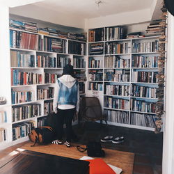 Rear view of woman standing by bookshelf