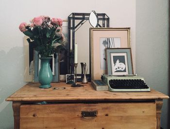 Flower vase and typewriter with frames on table at home