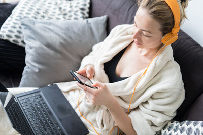 High angle view of woman listening music sitting on sofa at home