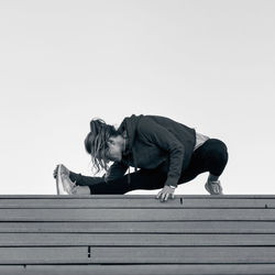 Full length of woman exercising on wood against clear sky