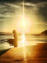 Side view of silhouette woman sitting at beach during sunset