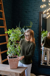 Young woman in green sweater taking care of the plants at home