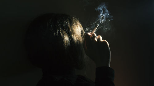 Rear view of man smoking against black background