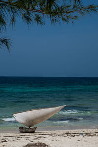 Boat moored at beach against clear blue sky