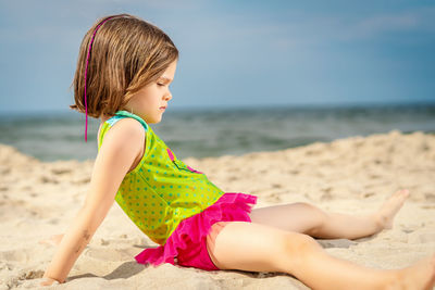 Girl relaxing on sand at beach against sky