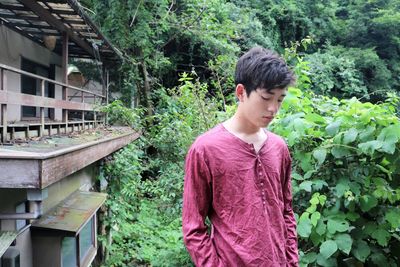 Side view of young man outside old house looking down