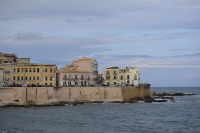 Buildings by sea against sky