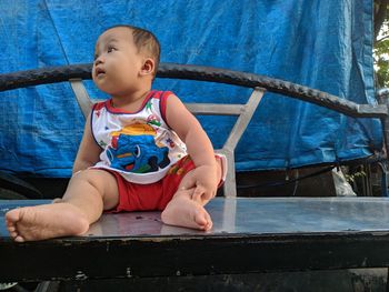 Cute boy looking away while sitting on blue wall