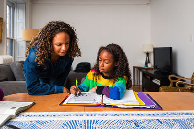 Mother assisting daughter in doing homework at table in living room