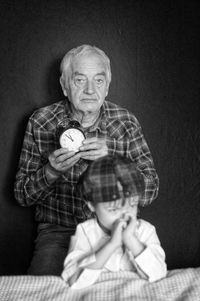 Portrait of old grandfather sitting behind a little boy and holding a clock