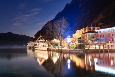 Illuminated buildings by lake against sky at night